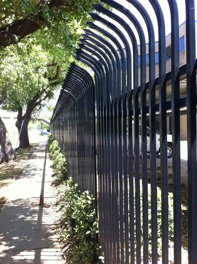 A dark bow-top decorative fence with scroll work running under trees
