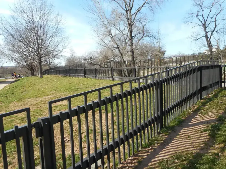 A black decorative park fence fabricated by Pool Custom Ironworks running down a slope
