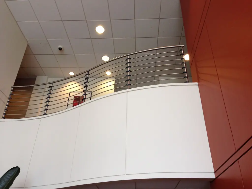 A curved cable railing on a white interior balcony against a red wall