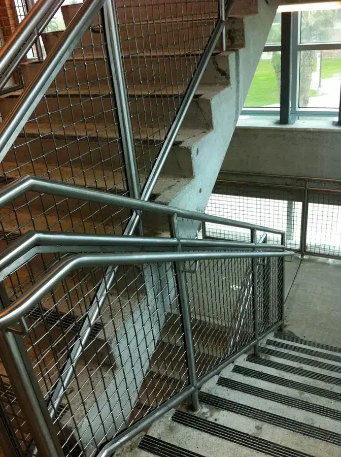 Stainless handrail with woven mesh infill panels beneath a concrete stair