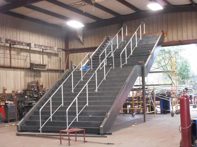 A gray monumental staircase with handrail standing finished in the Pool Custom Ironworks shop